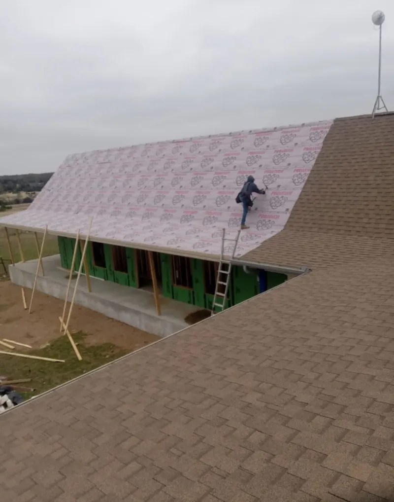 Worker preparing underlayment for a metal roof installation in West Athens